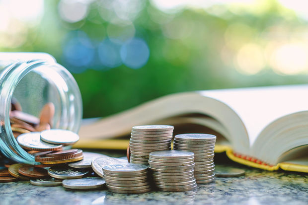 image-pile-of-money-coins-in-and-outside-the-glass-jar-on-blurred-book-and-natural-green-background-for-financial-and-education-concept